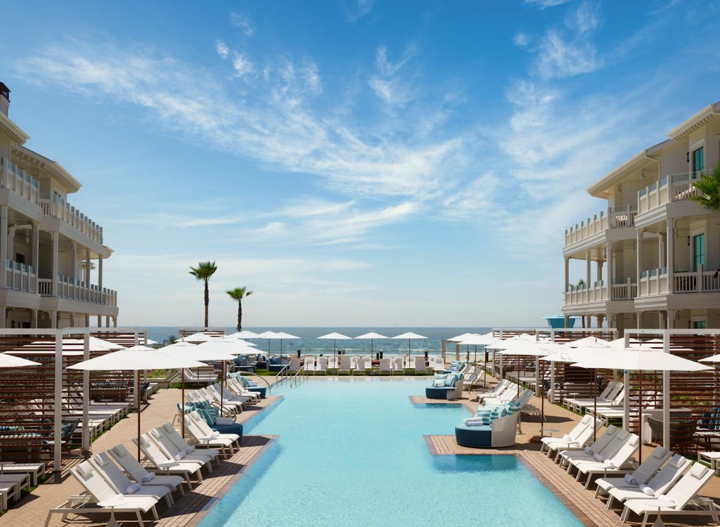 The pool between the white beachfront buildings of Shore House at The Del, with umbrellas and loungers
