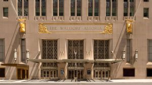 Front entrance of The Waldorf Astoria hotel with a gold sign and decorative reliefs above the doors.