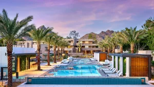 Arizona Biltmore pool lined with palm trees, white loungers and cabanas, with a mountain behind at dusk